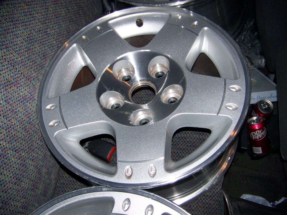 Bare silver five-spoke alloy wheel resting face-up on a cloth seat