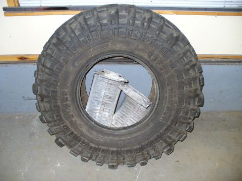 1978 Ford Bronco - A large, knobby tire sits on the floor, with two unidentifiable metal components placed within its rim.
