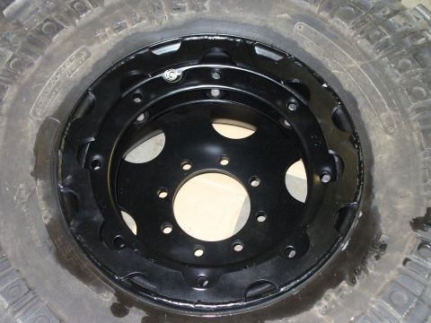 1978 Ford Bronco - A black steel wheel with a tire is shown, a beadlock-style ring and multiple lug holes.