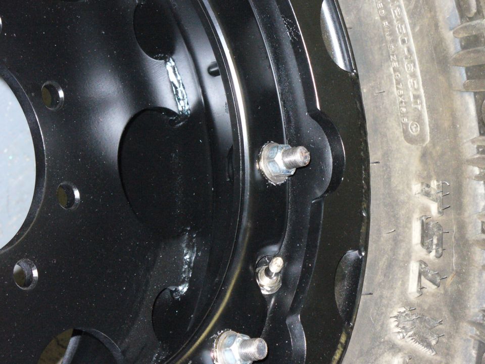 close-up of a black steel wheel with lug nuts and a tire sidewall visible