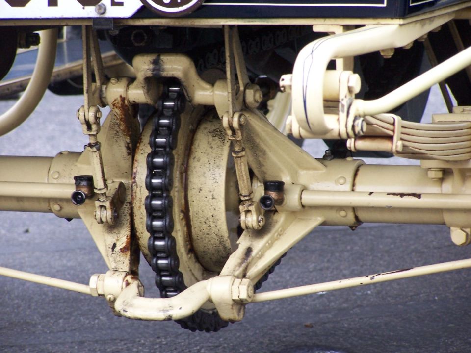 Underside of cream antique chain-drive rear axle with sprocket, roller chain and brake drum