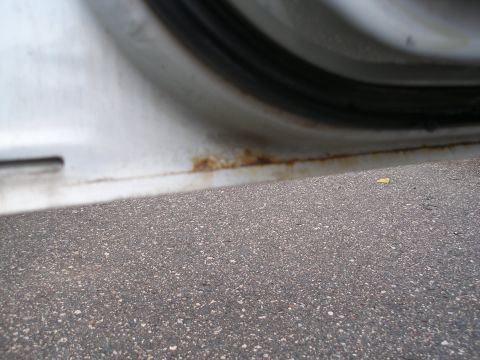 2000 Ford Crown Victoria - Rust is visible on the lower edge of a white car door sill, with asphalt below.