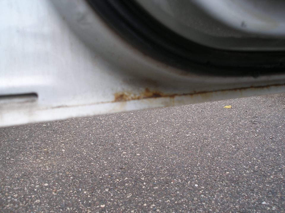 White car door sill with rust spots and asphalt in foreground