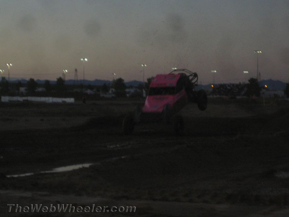 Pink off-road race buggy catching air over a dirt jump at dusk