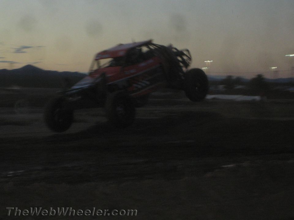 Red and black off-road race buggy jumping a dirt course at dusk