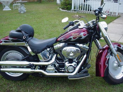1985 Ford Bronco - A maroon Harley-Davidson motorcycle with flame decals is parked on a grassy lawn, with a helmet resting on the seat.