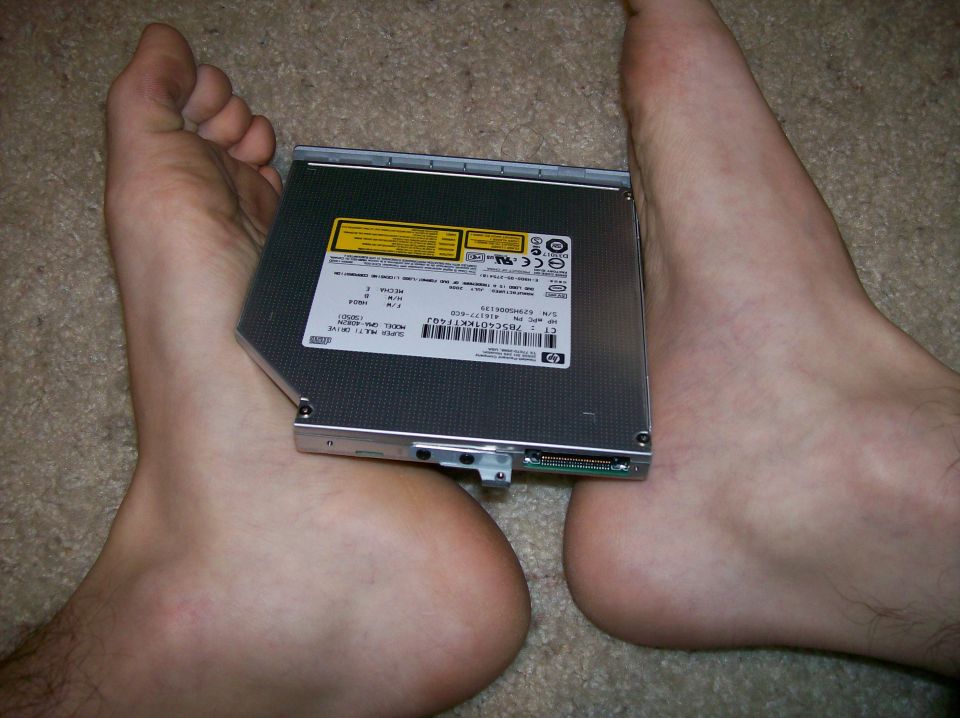 HP slim optical disc drive resting on a person's bare feet on carpet