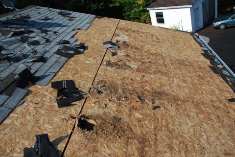 1996 Ford Bronco - A house roof undergoing repair, showing damaged shingles and exposed plywood, with a car parked nearby.