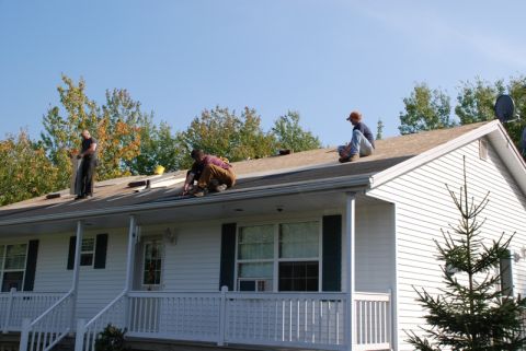 1996 Ford Bronco - Workers are seen on the roof of a house, performing repairs under a clear blue sky.