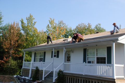 1996 Ford Bronco - Workers are seen on the roof of a white house, likely performing repairs or maintenance under a clear blue sky.