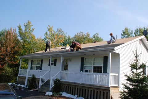 1996 Ford Bronco - Workers are on the roof of a house, performing repairs under a clear blue sky.