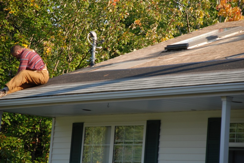 Man on roof during repairs, with trees and house visible