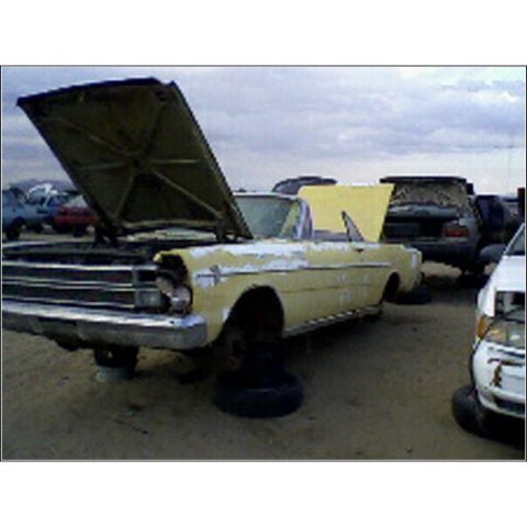 1973 Ford Ranchero - A yellow convertible sits in a junkyard with its hood open, surrounded by other vehicles under a cloudy sky.