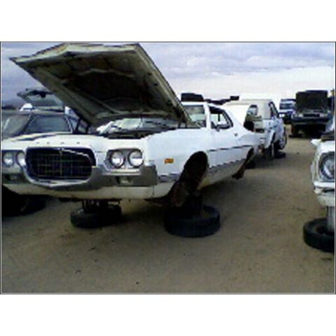1973 Ford Ranchero - A white 1972 Ford Gran Torino sits in a junkyard with its hood open and resting on tires.