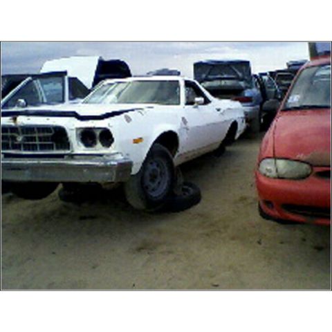 1973 Ford Ranchero - A white 1972 Ford Ranchero sits in a junkyard with its hood open and a missing front tire.