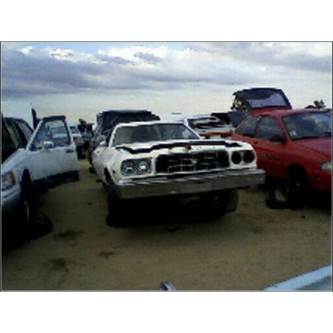 1973 Ford Ranchero - A white 1973 Ford Ranchero sits in a junkyard with other vehicles.