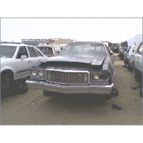 1973 Ford Ranchero - 1973 Ford Ranchero sits in a junkyard with a damaged front end and other cars nearby.