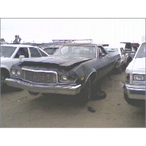 1973 Ford Ranchero - A dark coupe utility vehicle sits in a junkyard with a damaged front end and hood.