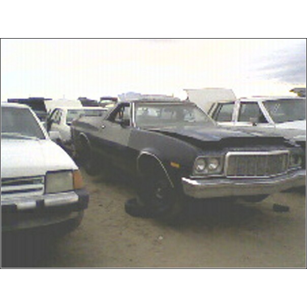 Dark blue 1972 Ford Ranchero with a dented hood and chrome grille, parked in a junkyard