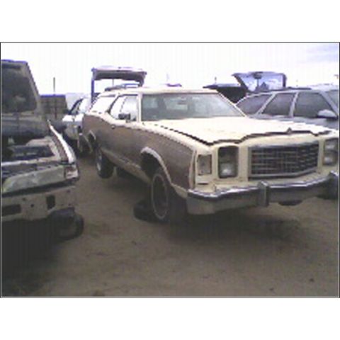 1973 Ford Ranchero - A beige station wagon with wood paneling sits in a junkyard, its front end facing the camera.