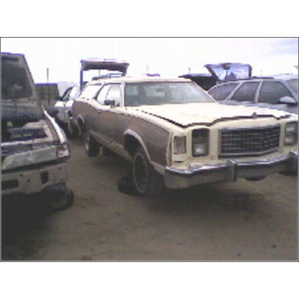 Beige station wagon with wood paneling, front end visible, in a junkyard