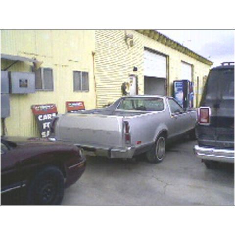 1973 Ford Ranchero - A silver pickup truck is parked in front of a commercial building with garage doors.