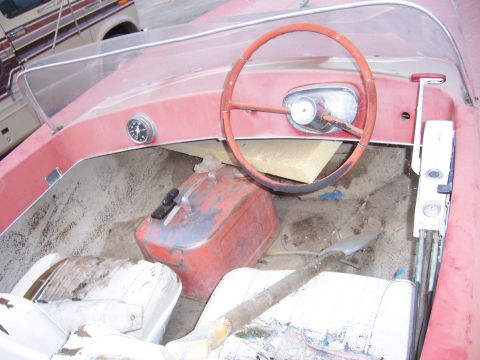 1991 Ford Bronco - The interior of a red boat shows a steering wheel, gas can, and worn seats.