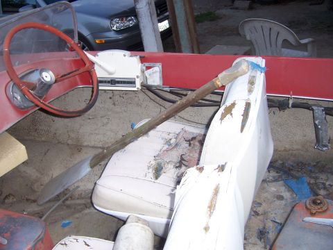 1991 Ford Bronco - The interior of a boat shows worn white seats, a red steering wheel, and a wooden oar.
