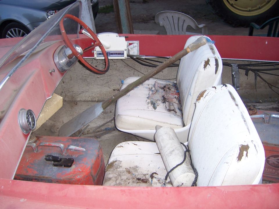 Interior of a red boat with white seats, steering wheel, and a paddle