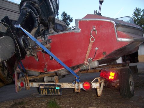 1991 Ford Bronco - A red boat is secured to a trailer with straps, showing its outboard motor and license plate.
