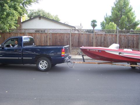1991 Ford Bronco - Pickup truck hauls a red boat on a trailer, seen from the side on a paved road.