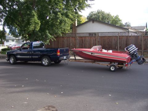 1991 Ford Bronco - A blue pickup truck tows a red boat on a trailer down a suburban street.