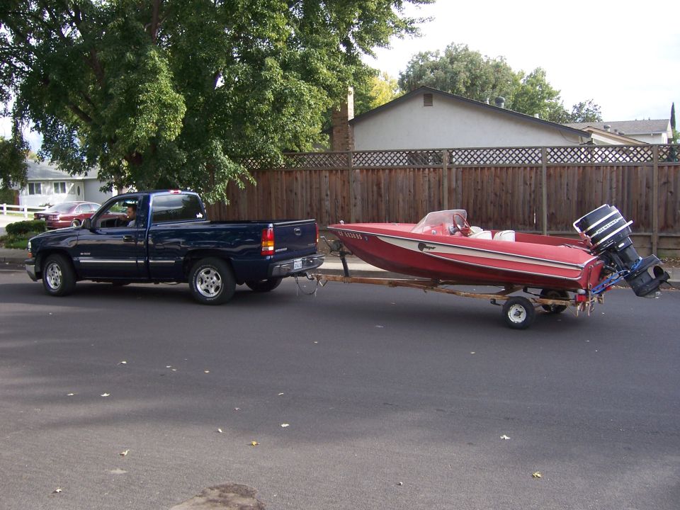 Blue pickup truck towing a red boat on a trailer down a residential street