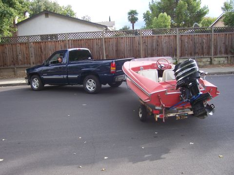 1991 Ford Bronco - A blue pickup truck tows a red boat on a trailer down a residential street.