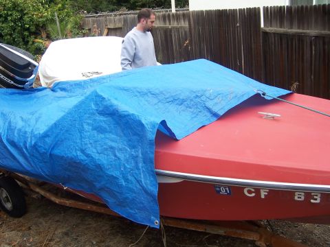 1991 Ford Bronco - A man stands next to a red boat covered by a blue tarp on a trailer.