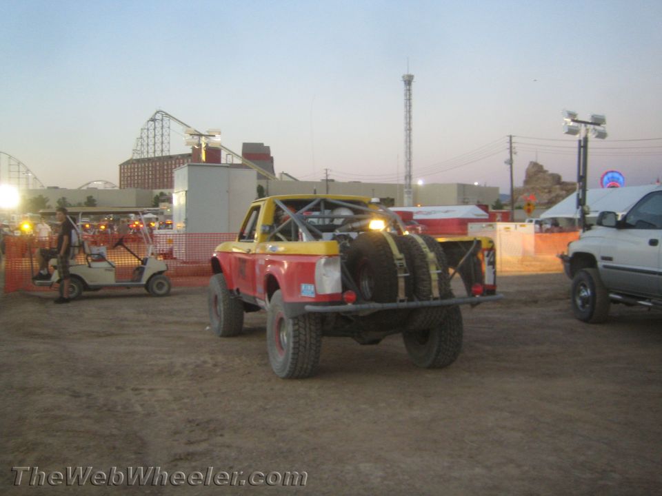 Rear of yellow and red off-road race truck with dual spare tires near a fairground
