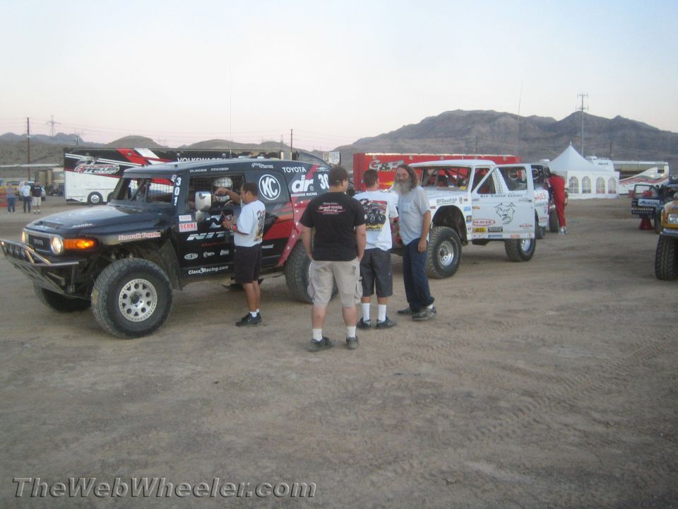 People standing around off-road race trucks in a desert pit area