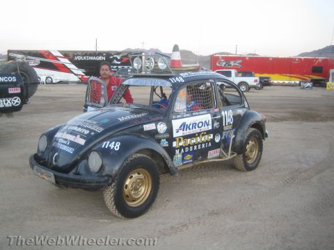 1990 Ford Bronco - black Volkswagen Beetle baja race car numbered 1148 with knobby tires and a roof light bar in a desert pit.