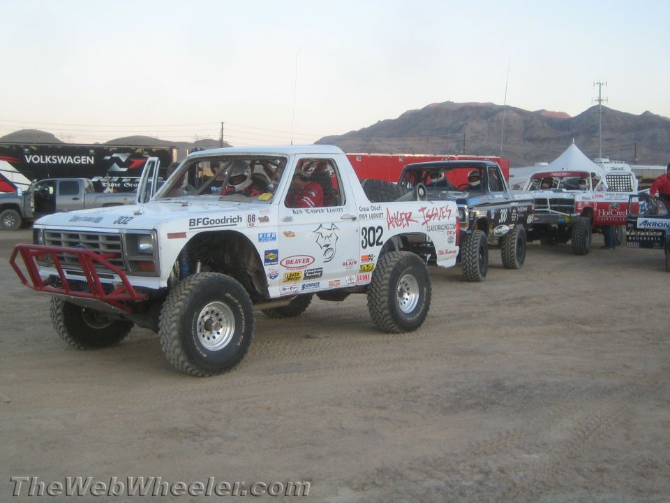 White Ford number 302 race truck staged with other trucks in desert pit
