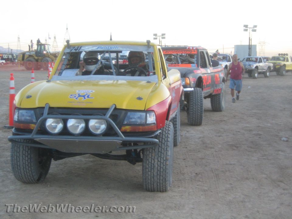 Yellow and red off-road race truck with triple lights on dirt at dusk