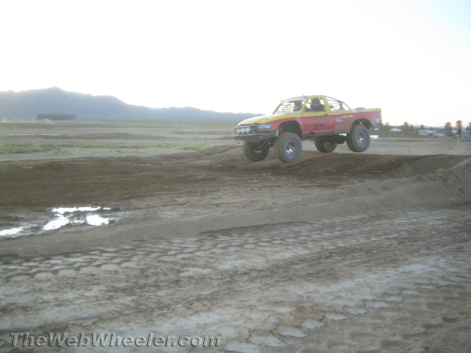 Red and yellow off-road race truck jumping over dirt mounds