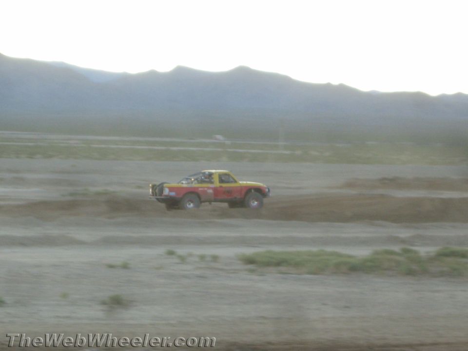 Red and yellow race truck speeding across the desert in dust