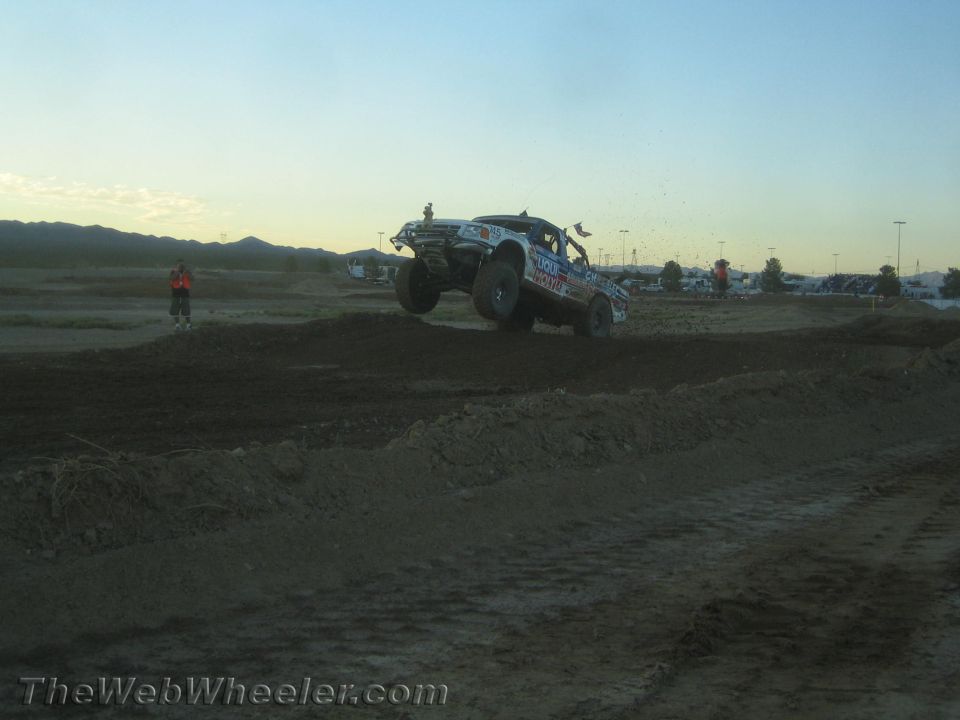 Off-road race truck catching air over a dirt jump at dusk