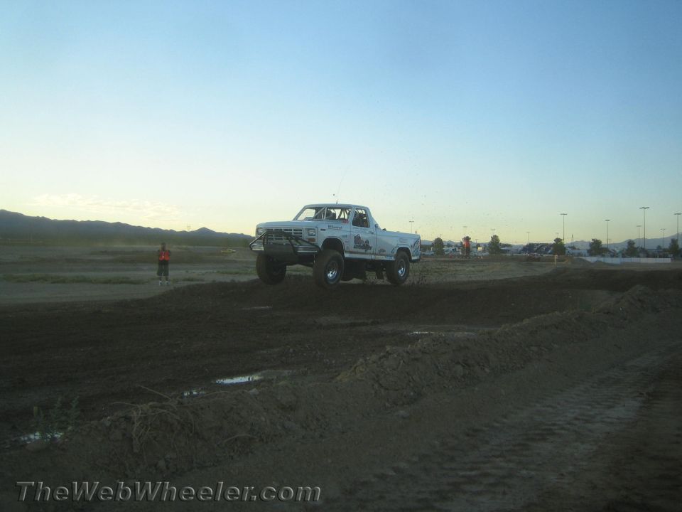 White lifted pickup truck jumping a dirt berm at dusk