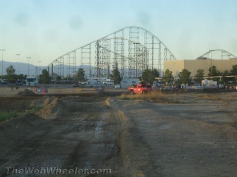 1990 Ford Bronco - red truck sits on a graded dirt course with a steel roller coaster and parking lot behind it.
