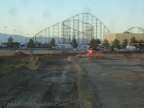 1990 Ford Bronco - red vehicle and parked trailers sit on a dirt course with a tall steel roller coaster in the background.