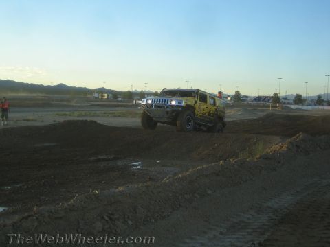 1990 Ford Bronco - yellow Hummer H2 crawls over a dirt berm on a desert off-road course at dusk.
