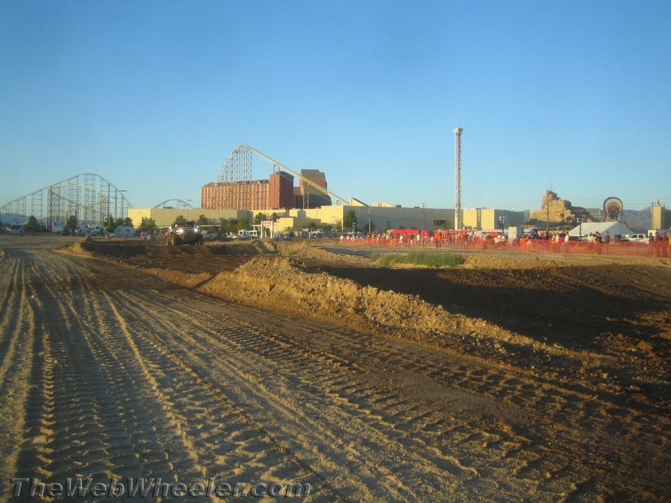 Graded dirt off-road course with buildings and a roller coaster behind