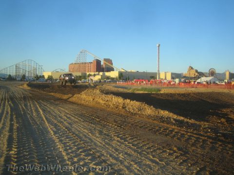 1990 Ford Bronco - dark pickup truck sits on a graded dirt course backed by buildings and a steel roller coaster.