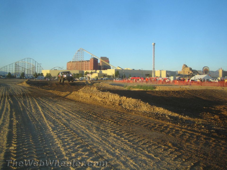 Dark pickup truck on a dirt course with a roller coaster backdrop